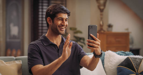istock Indian Man Using Video Call On Smartphone At Home: Doing Remote Work, Conducting Video Meetings with Clients. Young Man Cherishing Video Calls with His Girlfriend or Parents, Sharing Laughter and Love 1503330654