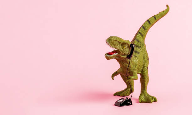 istock Cute green toy dinosaur speaking on retro phone on pink background. Copy space. 1503330663