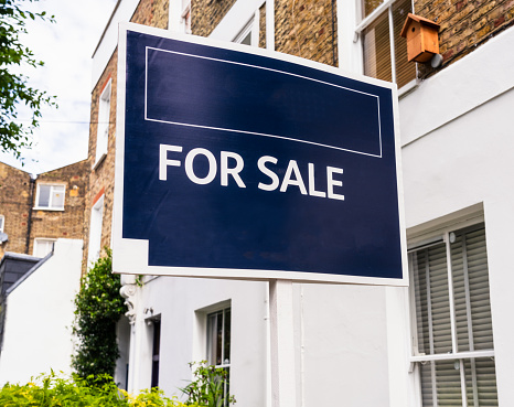 Close-up of a dark blue 'For Sale' estate agent's sign on a street in London, England.