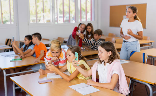 Schoolchildren use mobile phones at the lesson in classroom