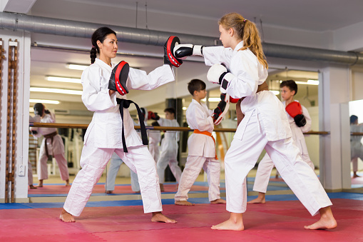 Female trainer in boxing gloves conducts sparring and teaches punches to a girl in karate and self-defense training