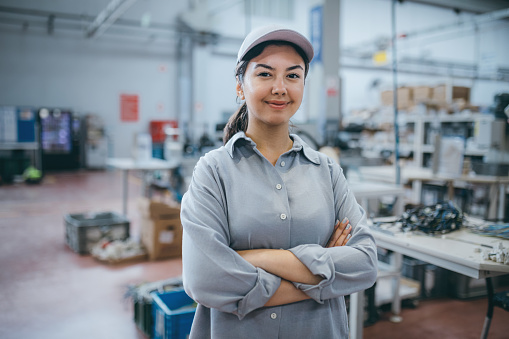 Portrait of trainee mechanic professional technical engineer businesswoman with blue coverall and eyeglass look at camera posing while standing, smiling, working in metal industry shipping manufacturing facility warehouse at metal cable factory with copy space area. XXXL size