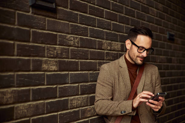 istock A businessman in a suit using a mobile phone while leaning on a brick wall. 1503345501