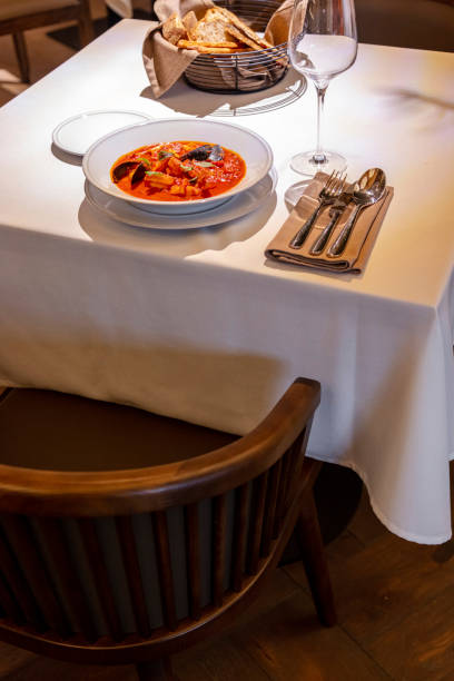 istock Tomato soup with seafood in a light ceramic plate. The soup is on a table with a light tablecloth, next to it is a glass of red wine and cutlery. 1503345727