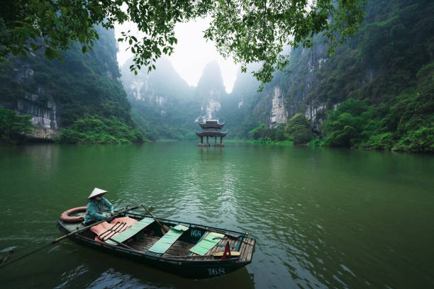 Boat rowing along the Thung Chuoi temple gate between karst mountains, Trang An, Ninh Binh, Vietnam Trang An, Vietnam - 11 April 2023: Boat rowing along the Thung Chuoi temple gate between lush green karst mountains high temple stock pictures, royalty-free photos & images