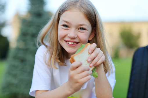 Close-up portrait of a laughing cute girl with a sandwich in her hands.