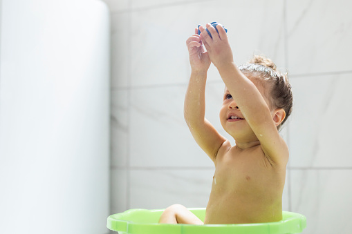 Beautiful child bathing and having fun in a basin at home