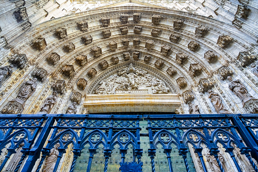 Milan Cathedral view of the top side columns, artwork and window with blue sky background from he roof walkway.