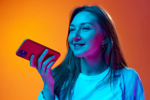 istock Smiling young woman recording voice message on mobile phone against gradient orange studio background in neon light. Online communication 1503354310