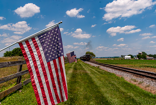 View of American Flags Waving on a Fence After a Steam Passenger Train Passed on a Sunny Summer Day