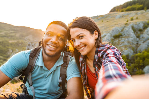 istock Smiling multiracial couple taking selfies while sitting on mountain peak 1503363318