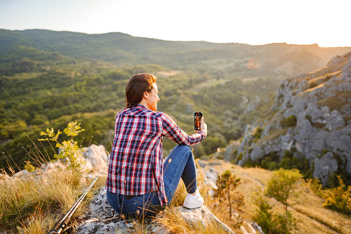 Young woman talking on a video call while sitting on a mountain peak with wonderful view