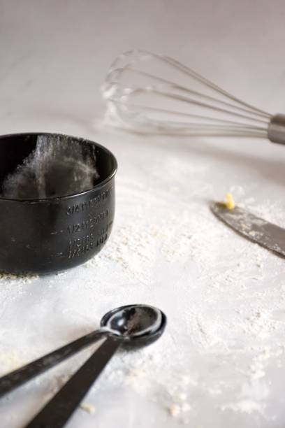 istock Closeup of two black measuring spoons with other baking tools on a table covered in flour. 1503364765