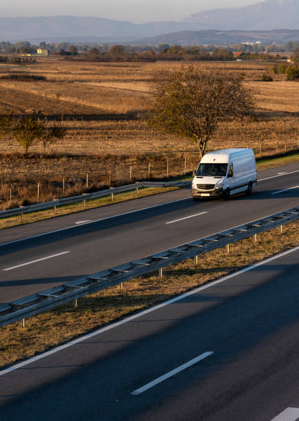 white delivery van on the highway. white modern delivery small shipment cargo courier van moving fast on motorway road to city urban suburb. the world's best transport of goods. - delivery van imagens e fotografias de stock