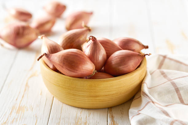Fresh raw onion ready for cooking. Wooden plate with onion shallots on white table. stock photo