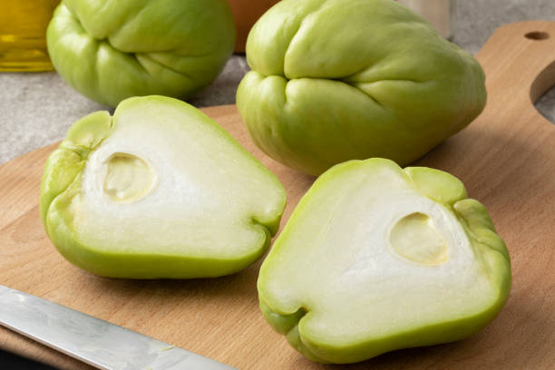 Whole and halved fresh chayote on a cutting board Whole and halved fresh chayote on a cutting board close up Christophine stock pictures, royalty-free photos & images