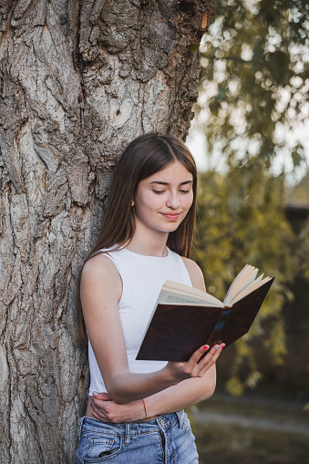 A teenage girl reading a book in nature. Beautiful girl immerses herself in a book while enjoying the natural surroundings. It reflects the idea that reading can transport us to different places and moments, while finding peace and connection with nature.