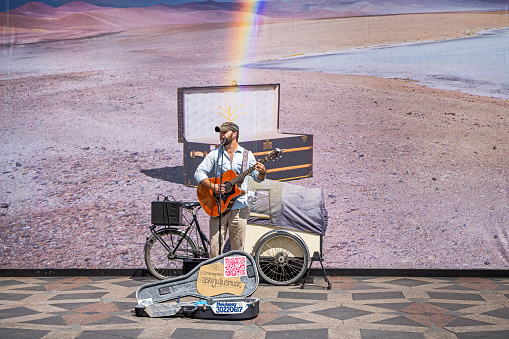 Copenhagen, Denmark - June 24th 2023: Street musician standing in front of an advertisement poster with a rainbow in the center of the Danish capital
