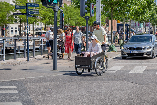 Copenhagen, Denmark - June 24th 2023: Young couple driving round a a street corner on a cargo bike in the center of the Danish capital - cargo bikes are a very popular way of transport as an alternative to cars in most big cities