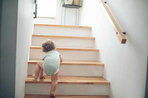 Little cute toddler girl climbing on stairs at home
