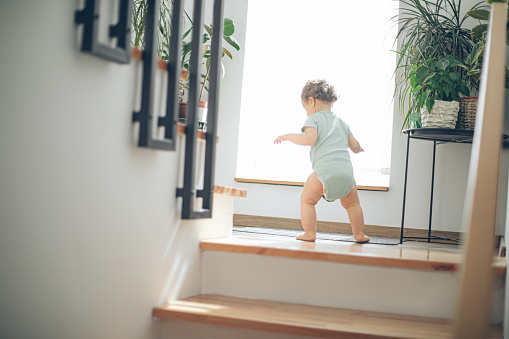 Little cute toddler girl climbing on stairs at home