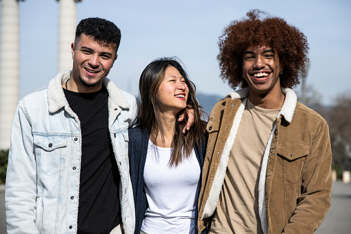 Three happy young people smiling and looking relaxed in the street. Group of millennials staring at camera laughing outdoors.