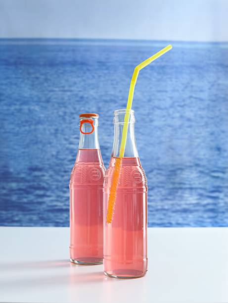Two bottles of vibrant pink soda displayed on a table overlooking a beautiful beach