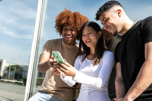 istock Three young diverse people looking at a smartphone standing int the street.Two young men smiling and watching at the phone of a happy woman. 1503372946