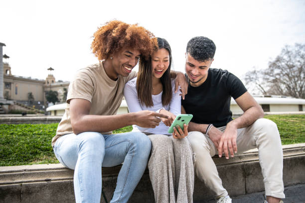 istock Three young diverse people looking at a smartphone sitting on a park.Two young men smiling and pointing at the phone of a happy woman. 1503372970