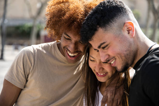 istock Diverse group of friends hugging together and smiling confident. Three relaxed young persons looking down and laughing outdoors. 1503372994