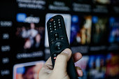 Male hand holding remote control tv screen with the website blurred in the background.