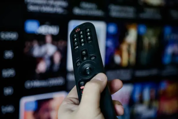 Male hand holding remote control tv screen with the website blurred in the background.