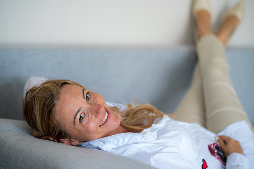 Happy woman lying on the sofa and looking at camera at home
