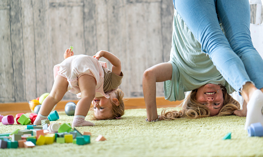 Happy mother and her little daughter standing upside down on the carpet at home