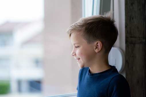 Happy little boy day dreaming while looking through window