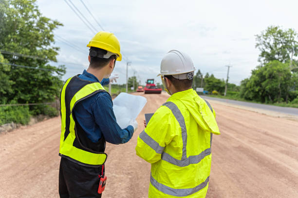 Asian engineer holding tablet and foreman holding road construction blueprints, on construction site to supervise road construction In the background is a road under construction and machinery working ingeniero asiático sosteniendo tableta y capataz sosteniendo planos de construcción de carreteras, en el sitio de construcción para supervisar la construcción de carreteras en el fondo hay una carretera en construcción y maquinaria en funcionamiento