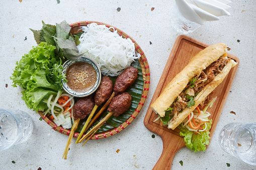Taste of Vietnam. Traditional vietnamese food on table in restaurant. Pork meatballs, noodles, salad and Banh mi Sandwich.