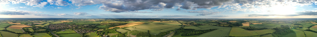 A panoramic view of a green open agricultural field surrounded by a cloud-filled sky