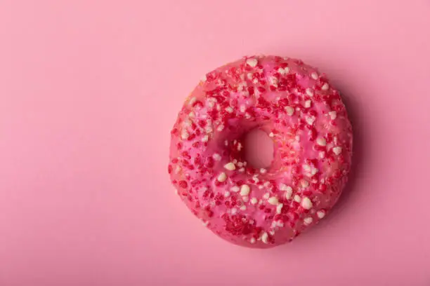 Donut on a pink background.Strawberry donut with pink icing and sprinkles on a paper background.Colorful minimalism concept.Junk food.Sweets.Copy space.Flat lay.Place for text.