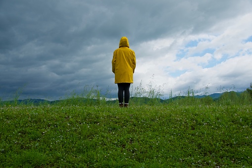 Girl look at cloudy sky weather from behind with yellow raincoat