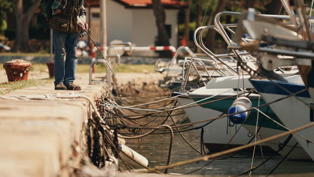 SLO MO Unknown One-Handed Man Fishing at a Slovenian Coast Harbor Amidst Moored Boats