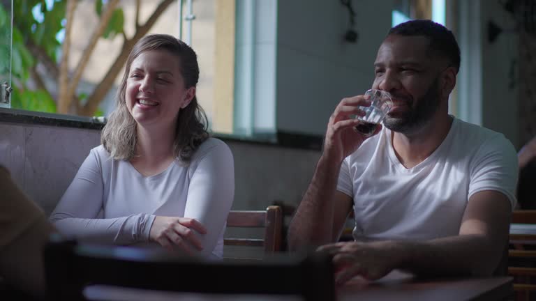 Candid diverse friends meeting sitting at restaurant table. Man and woman at Brazilian cafeteria get together interaction and socializing at small business