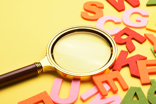 Multi colored alphabet letters and magnifying glass on the yellow background with copy space