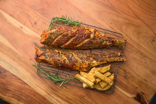 An overhead shot of two pieces of fish on a metal grill tray accompanied with fries and rosemary