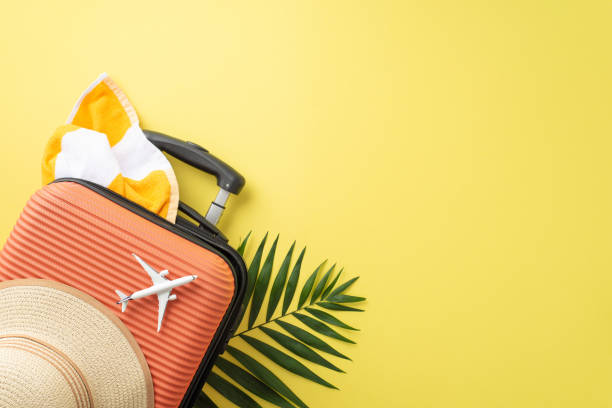 istock Dive into summer bliss! Glimpse top view suitcase, miniature airplane, beach essentials like sunhat, towel, and palm leaves on yellow backdrop. Unleash your travel advertising potential in open space 1503434372
