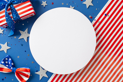 Patriotic joy on Independence Day. Top view presents display of symbolic items, stars, confetti, bow-tie, giftbox wrapped perfectly, arranged on USA flag backdrop with circle, ideal for text or advert
