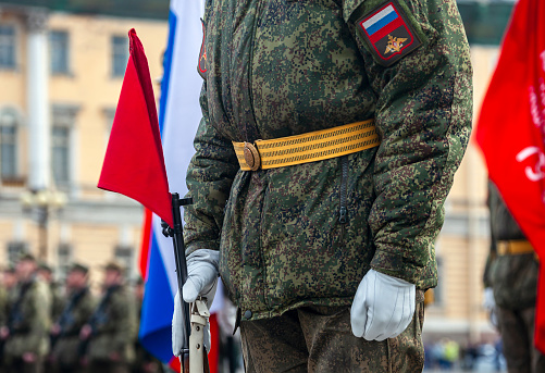Field military uniform of Russian soldier at parade rehearsal against the background of the colors of the national flag. Details of clothing and equipment of an officer with weapon at parade training on Palace Square in St. Petersburg.