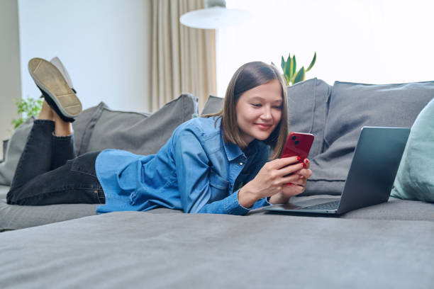 istock Young happy woman using smartphone laptop, lying on sofa at home 1503439813