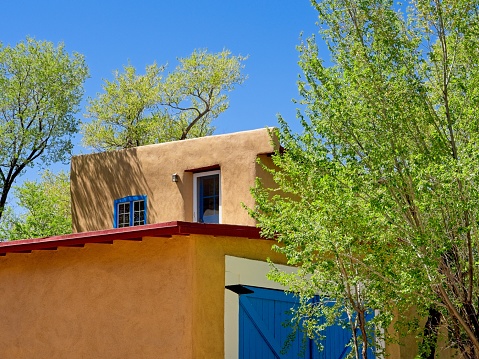 Taos, New Mexico - USA, May 12, 2023. Adobe structure roofline with green tree and blue sky background in Taos, New Mexico.