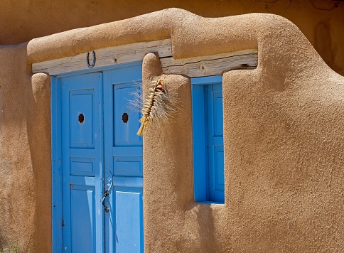 Taos, New Mexico - USA, May 12, 2023. Blue doorway contrasts with earth toned adobe church building in Rancho de Taos New Mexico.